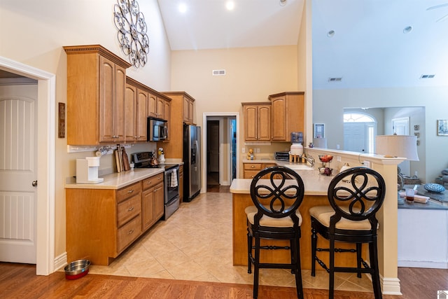 kitchen with a breakfast bar, kitchen peninsula, sink, appliances with stainless steel finishes, and light tile patterned floors