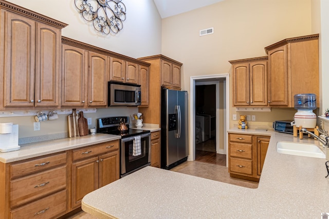 kitchen with a high ceiling, sink, appliances with stainless steel finishes, and a chandelier