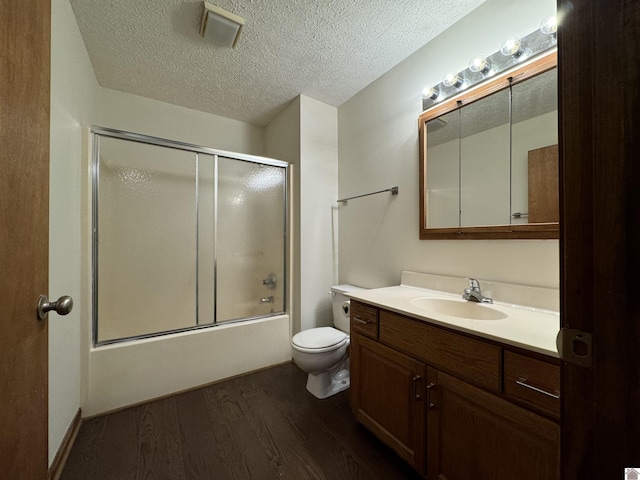 full bathroom with a textured ceiling, wood-type flooring, vanity, bath / shower combo with glass door, and toilet