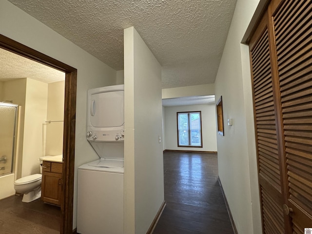 corridor featuring a textured ceiling, dark wood-type flooring, and stacked washer / dryer