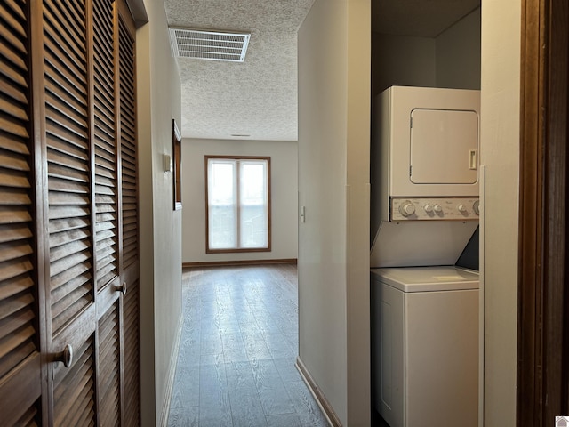 laundry area with stacked washer and dryer, a textured ceiling, and light hardwood / wood-style flooring