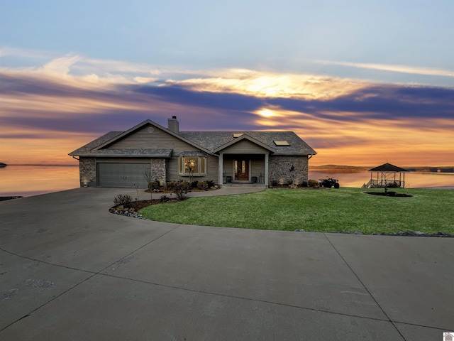 view of front of house with a garage, a water view, and a lawn