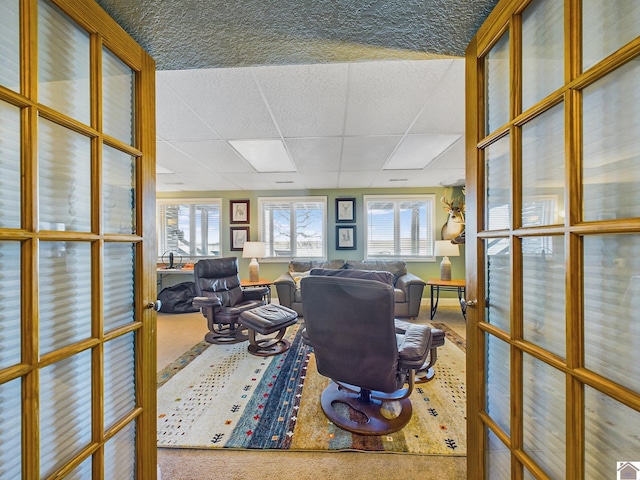 carpeted office with a healthy amount of sunlight, a drop ceiling, and french doors