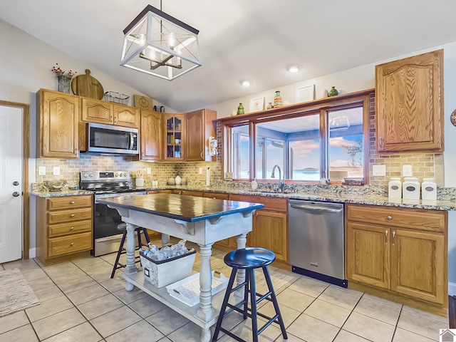 kitchen featuring appliances with stainless steel finishes, lofted ceiling, a notable chandelier, light tile patterned flooring, and light stone counters