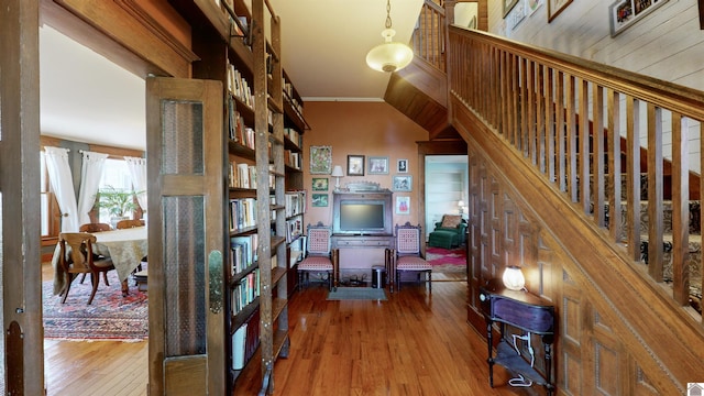 corridor with hardwood / wood-style floors, crown molding, wood walls, and vaulted ceiling