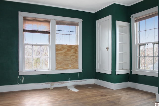 empty room featuring plenty of natural light, wood-type flooring, and ornamental molding