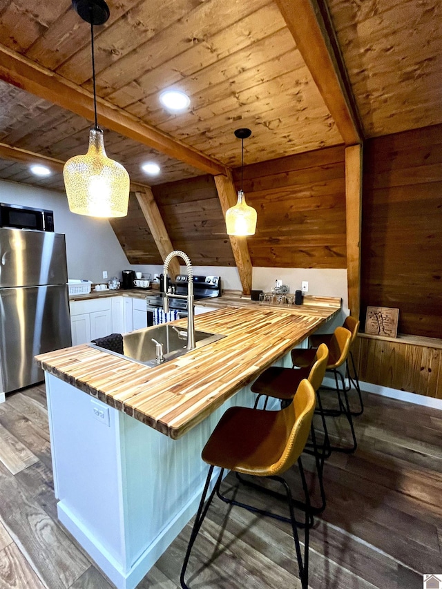 kitchen featuring kitchen peninsula, butcher block countertops, stainless steel appliances, pendant lighting, and white cabinets