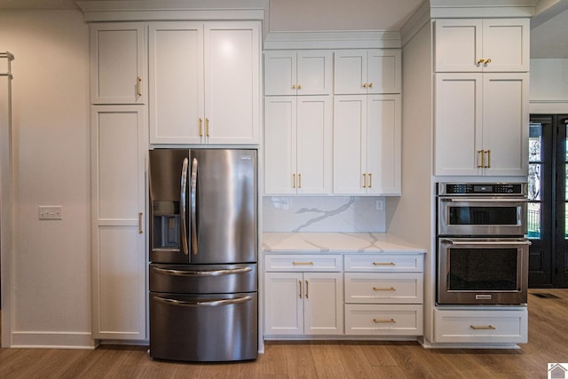 kitchen featuring tasteful backsplash, light wood-type flooring, light stone countertops, appliances with stainless steel finishes, and white cabinets