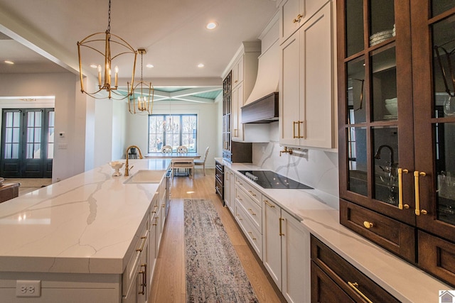 kitchen with pendant lighting, white cabinets, black electric stovetop, sink, and a large island