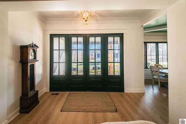 entryway with wood-type flooring, ornamental molding, french doors, and an inviting chandelier