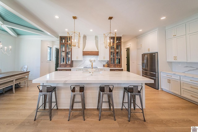 kitchen featuring decorative light fixtures, custom exhaust hood, a large island, white cabinets, and stainless steel fridge