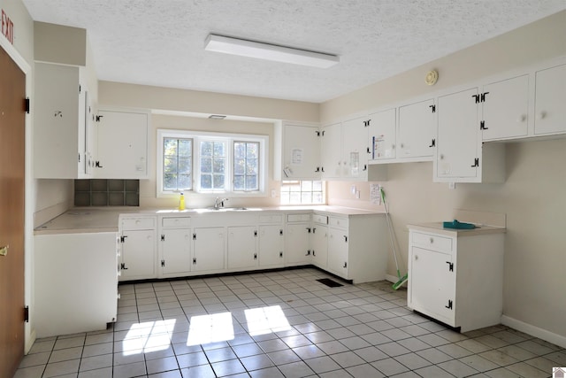 kitchen featuring white cabinets, sink, light tile patterned floors, and a textured ceiling