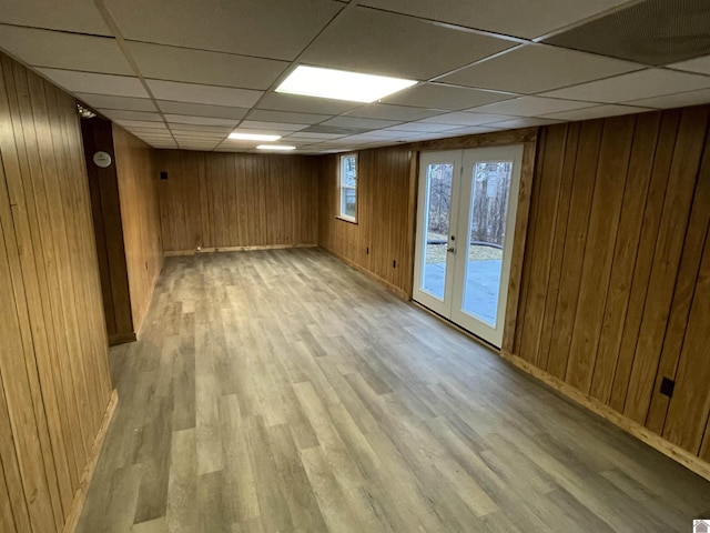 basement with a drop ceiling, wood walls, and french doors