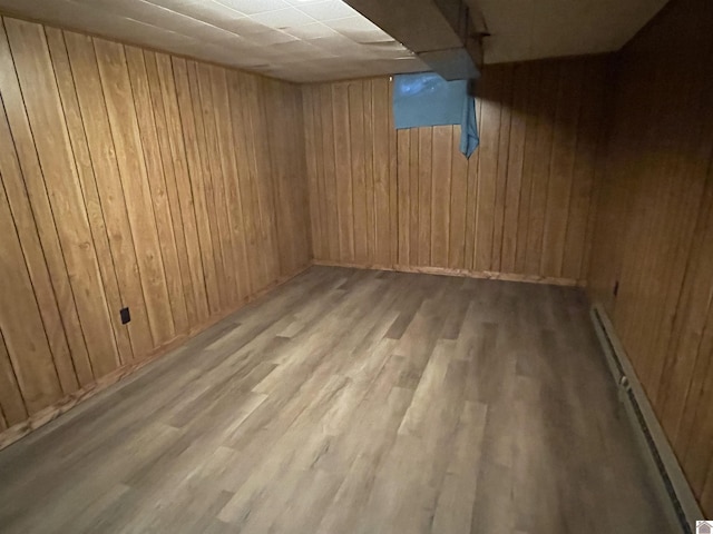 basement featuring a baseboard heating unit, wood walls, and light wood-type flooring