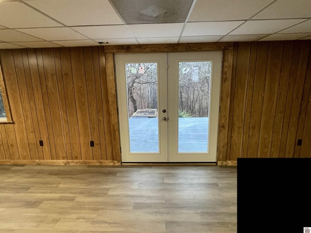 doorway featuring light wood-type flooring, french doors, a drop ceiling, and wood walls