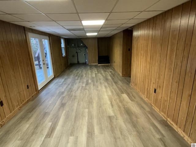 basement featuring light hardwood / wood-style floors, wood walls, and french doors