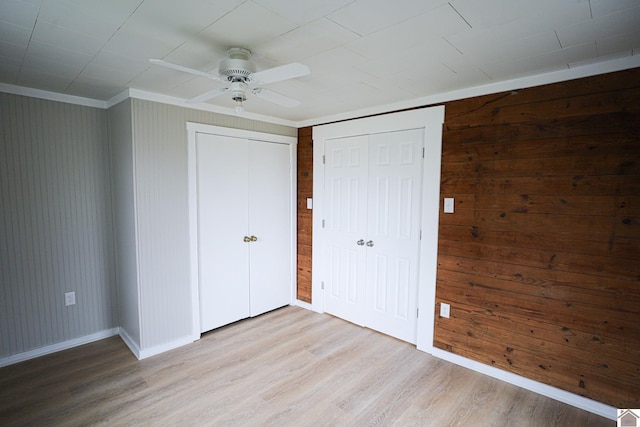 unfurnished bedroom with ceiling fan, light wood-type flooring, wood walls, and ornamental molding