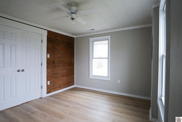 unfurnished bedroom featuring ceiling fan, light wood-type flooring, wood walls, and crown molding