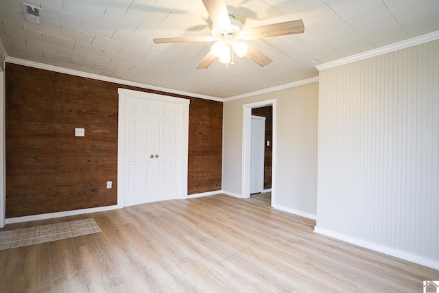 unfurnished bedroom with ceiling fan, wooden walls, light hardwood / wood-style flooring, ornamental molding, and a closet