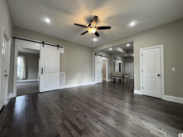 unfurnished living room with ceiling fan, a barn door, dark hardwood / wood-style flooring, and a textured ceiling