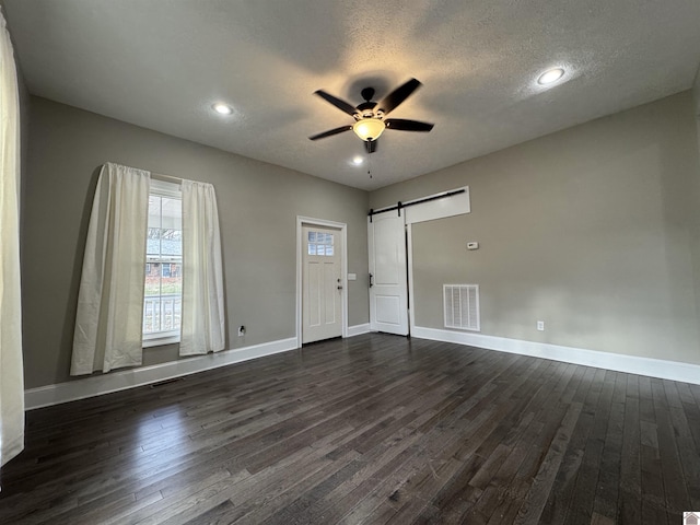 empty room featuring a textured ceiling, dark wood-type flooring, a barn door, and ceiling fan