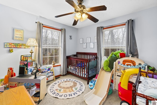 carpeted bedroom featuring ceiling fan and a crib