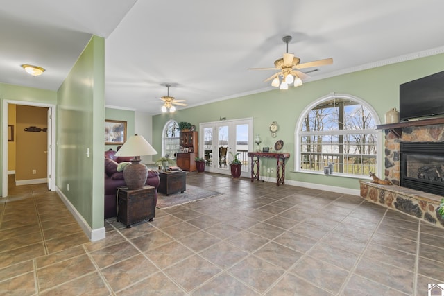 living room with ceiling fan, ornamental molding, french doors, and a stone fireplace