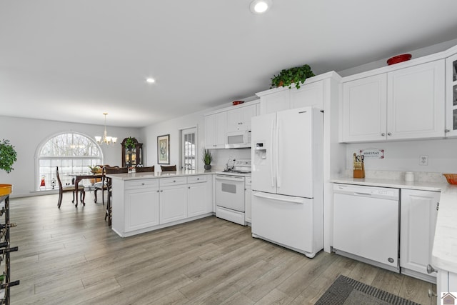 kitchen with an inviting chandelier, kitchen peninsula, white appliances, pendant lighting, and white cabinets