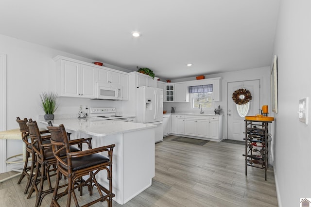 kitchen featuring white cabinetry, kitchen peninsula, white appliances, light hardwood / wood-style flooring, and a breakfast bar