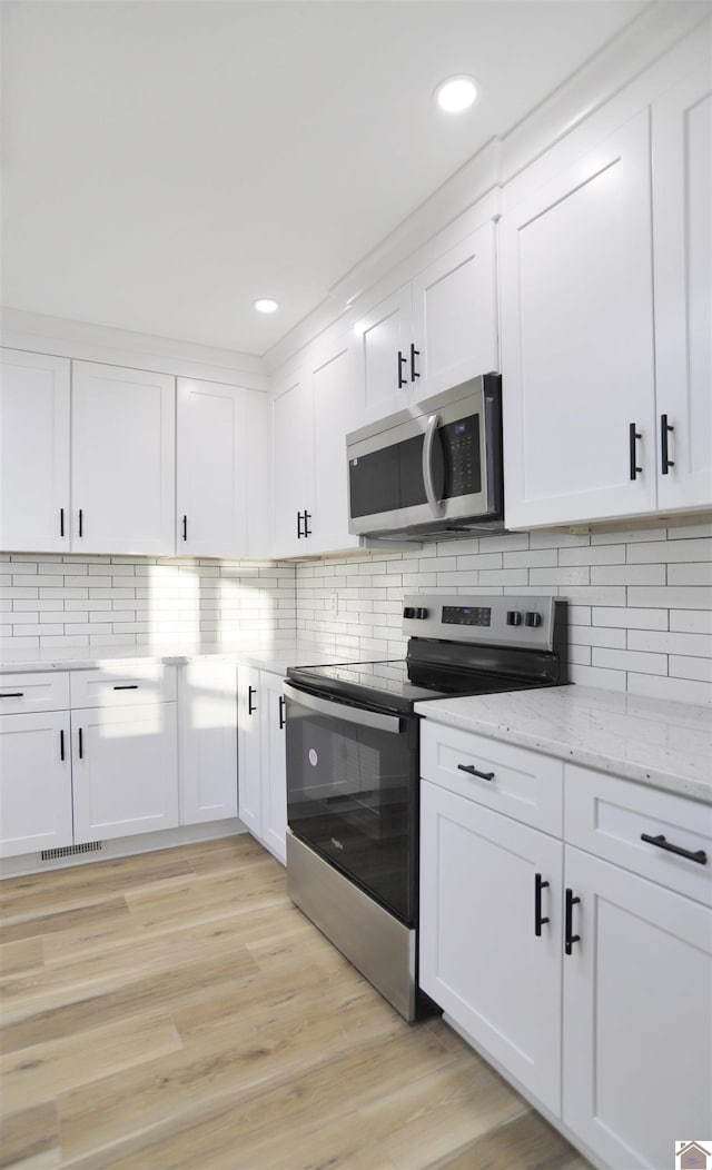 kitchen with decorative backsplash, white cabinetry, appliances with stainless steel finishes, and light wood-type flooring