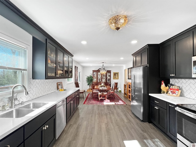 kitchen featuring stainless steel appliances, tasteful backsplash, sink, hanging light fixtures, and light wood-type flooring