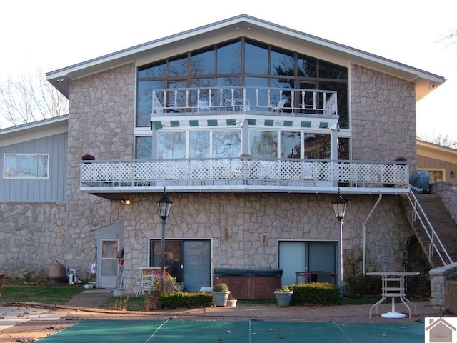 rear view of property with a balcony and a hot tub