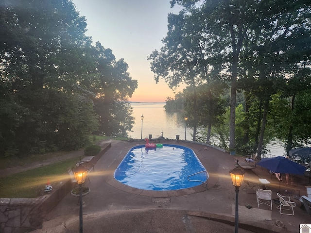 pool at dusk featuring a water view and a patio