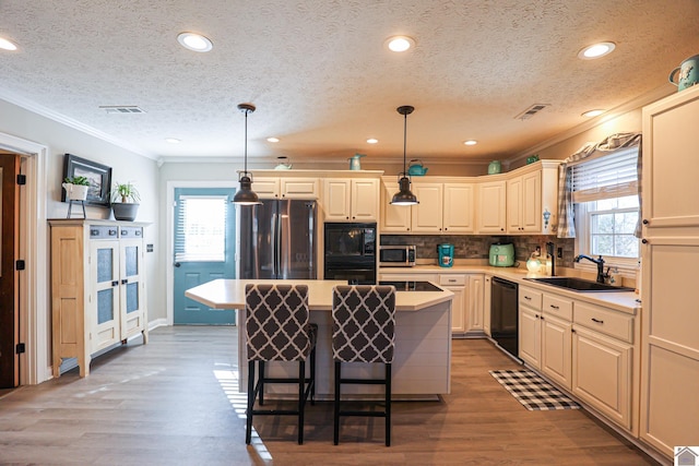 kitchen featuring decorative light fixtures, black appliances, sink, and a center island