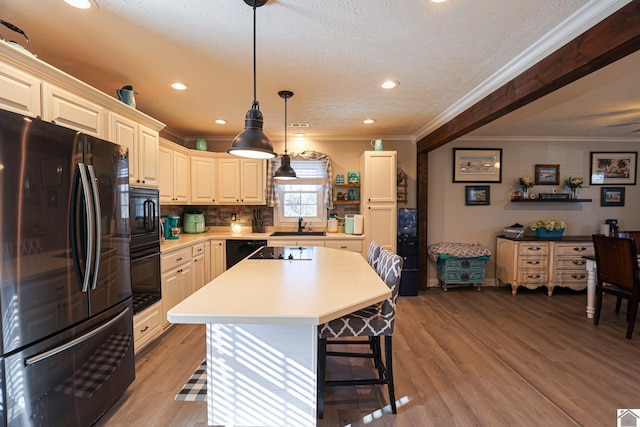 kitchen with a kitchen breakfast bar, light wood-type flooring, hanging light fixtures, black appliances, and a center island