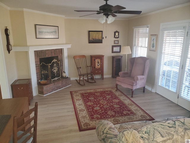 living room featuring light wood-type flooring, ceiling fan, crown molding, and a fireplace