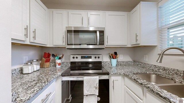 kitchen with appliances with stainless steel finishes, white cabinetry, light stone counters, and sink