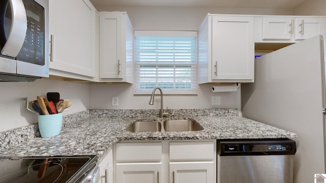 kitchen with appliances with stainless steel finishes, white cabinetry, light stone counters, and sink