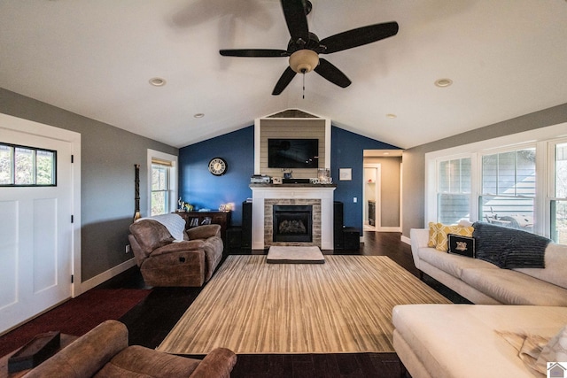 living room with vaulted ceiling, a stone fireplace, ceiling fan, and dark wood-type flooring