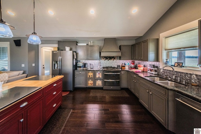 kitchen featuring pendant lighting, wall chimney range hood, stainless steel appliances, tasteful backsplash, and sink