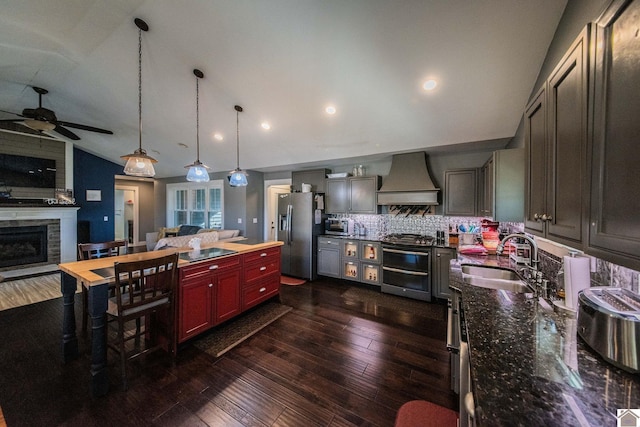 kitchen with appliances with stainless steel finishes, wall chimney exhaust hood, tasteful backsplash, sink, and vaulted ceiling