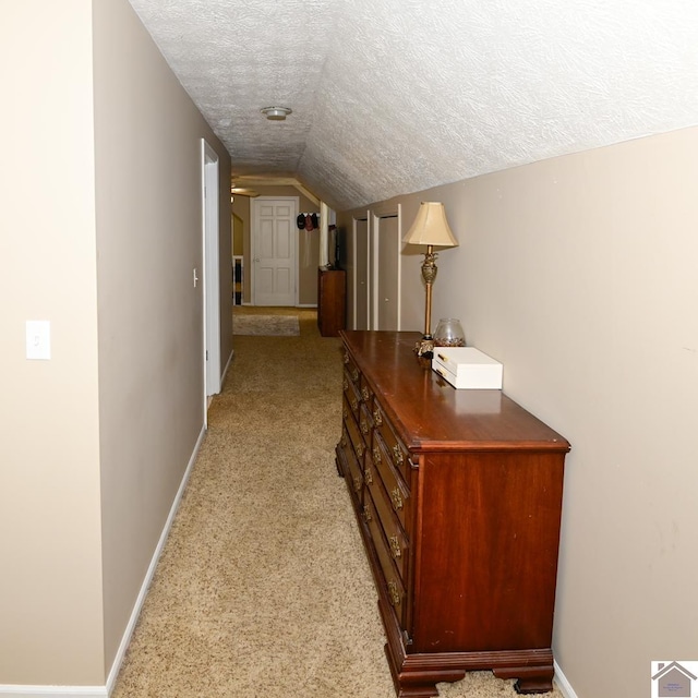 hall featuring light colored carpet, a textured ceiling, and vaulted ceiling