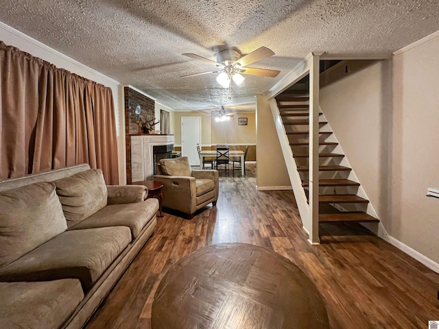 living room with a textured ceiling, wood-type flooring, a fireplace, ceiling fan, and crown molding