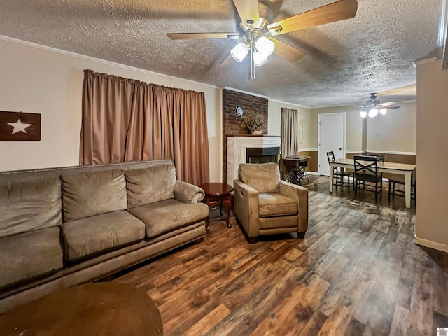 living room with crown molding, a textured ceiling, a brick fireplace, dark wood-type flooring, and ceiling fan