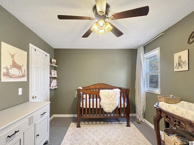 bedroom with ceiling fan, a textured ceiling, a nursery area, and light carpet