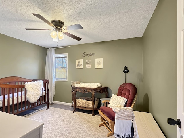 bedroom with ceiling fan, light colored carpet, a textured ceiling, and a crib