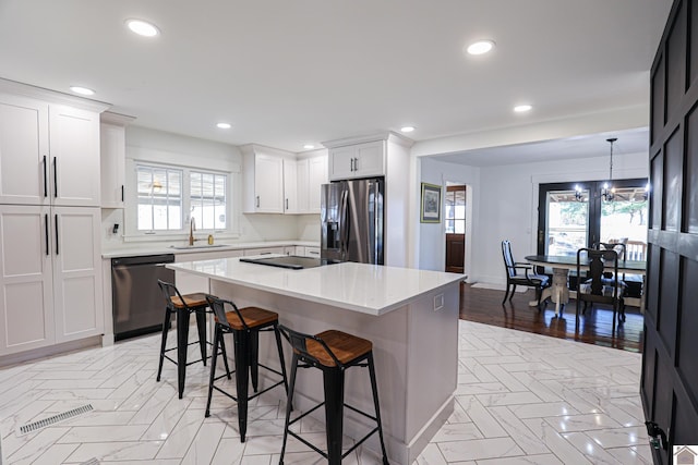 kitchen with hanging light fixtures, white cabinets, a kitchen bar, a kitchen island, and black appliances