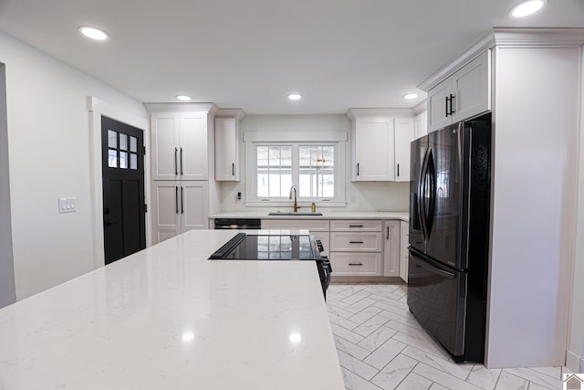 kitchen with sink, black refrigerator, white cabinets, and light stone countertops