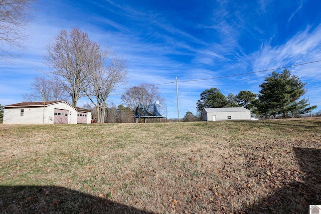 view of yard with a garage, an outbuilding, and a trampoline