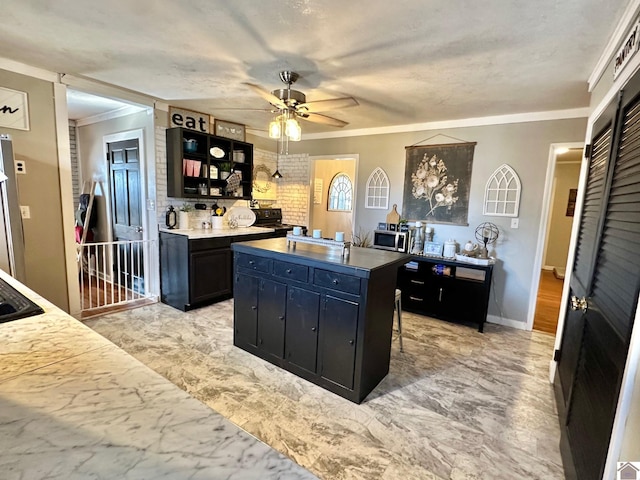 kitchen featuring a kitchen bar, ornamental molding, ceiling fan, and a kitchen island